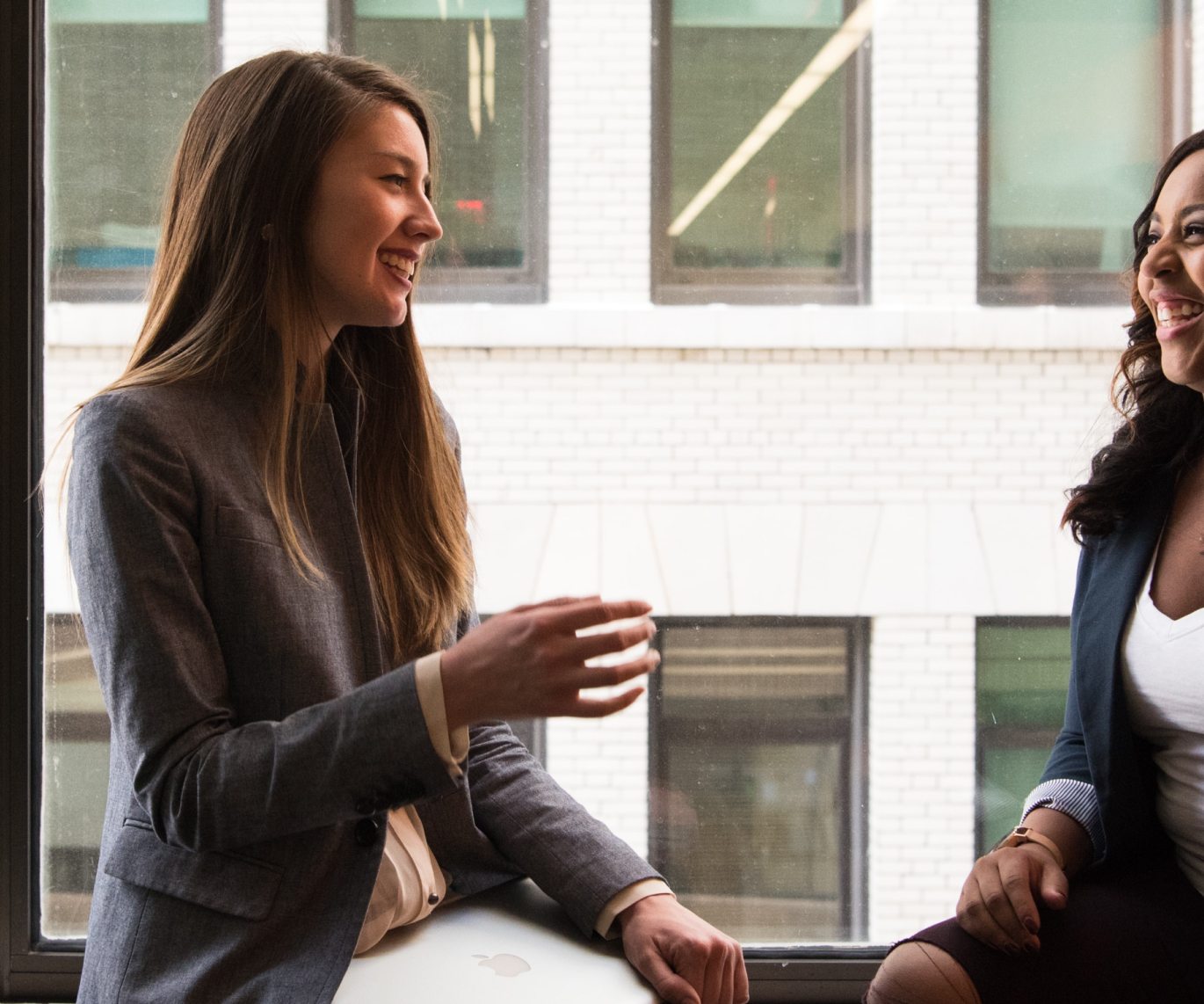 Two businesswomen talking to each other and laughing.