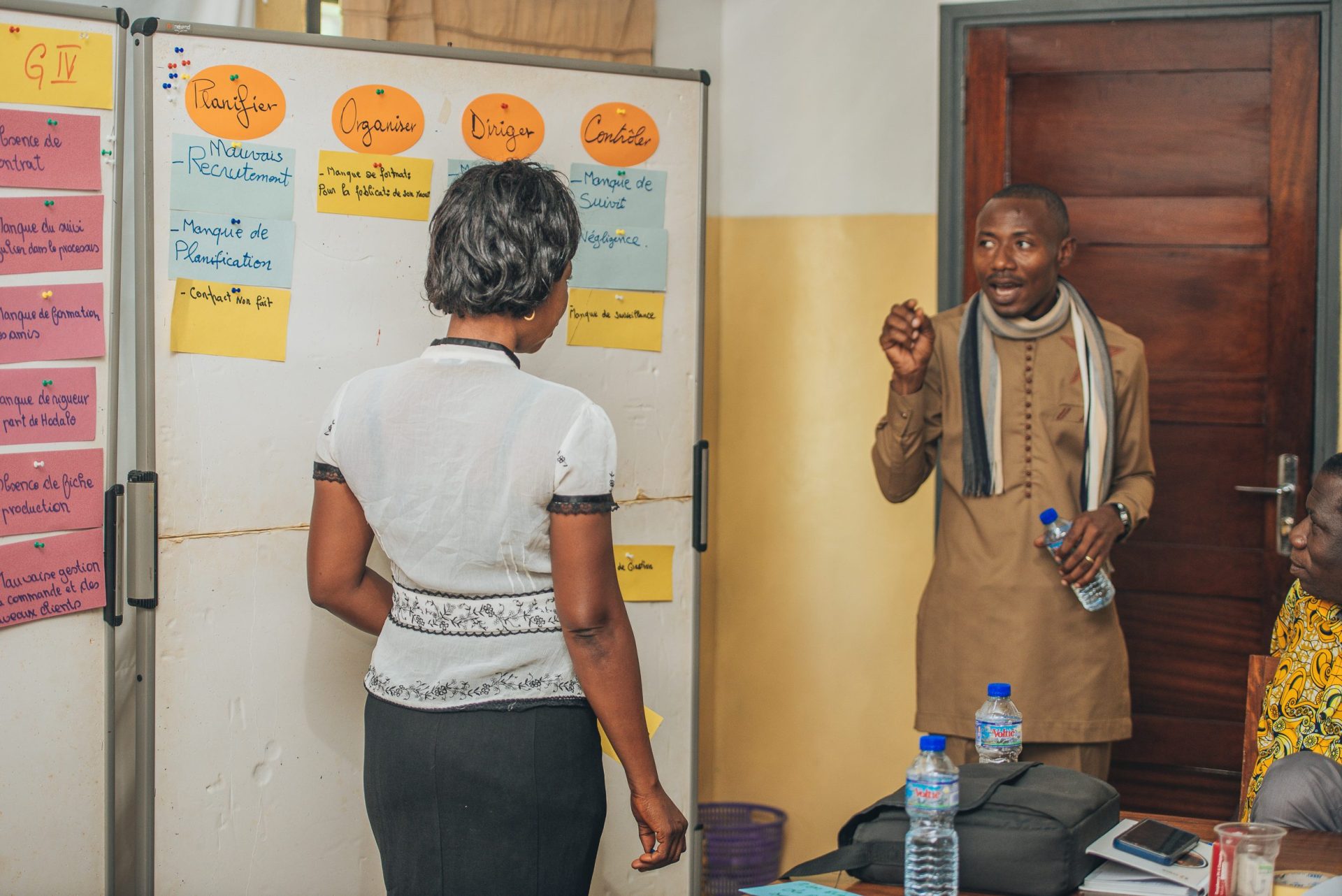 A trainer moderating a session whila a female partcipant is standing at a whiteboard.