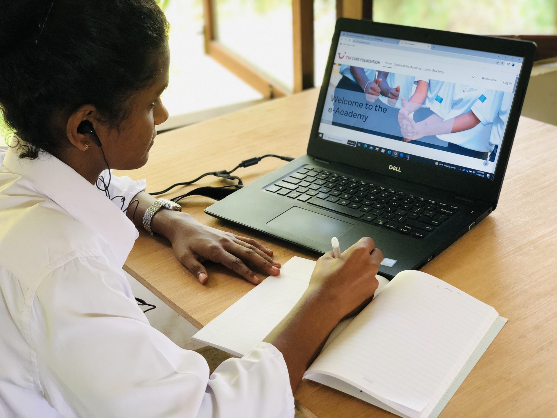 A lady using the atingi e-learning platform and writing notes.